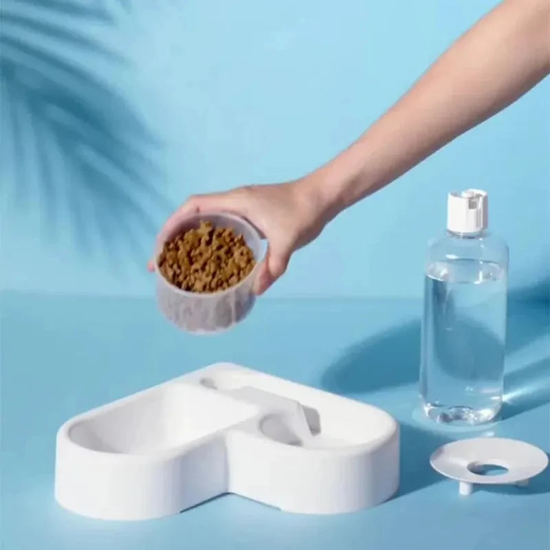 Pet feeding station with a hand holding a bowl of food, water bottle, and additional dish on a blue background.
